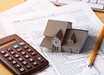 A small model of a house on top of papers with a pencil and calculator next to it